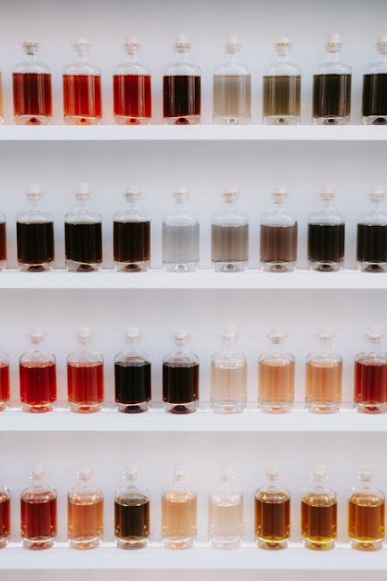 Vibrant rows of various colored liquids in glass bottles arranged neatly on white shelves.